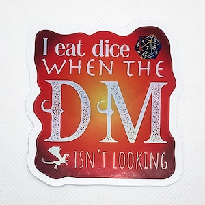 May include: A red and orange sticker with a white border and the text "I eat dice when the DM isn't looking". A white dragon is in the bottom left corner and a multi-colored 20-sided die is in the top right corner.