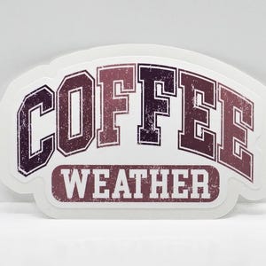 May include: White sticker with the text "COFFEE WEATHER" in a distressed, vintage-style font. The letters are in shades of purple and pink.