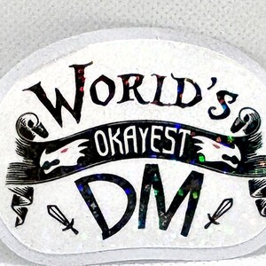 May include: White oval sticker with black text and a black and white illustration of a banner with a dragon on each end. The text reads "World's Okayest DM".