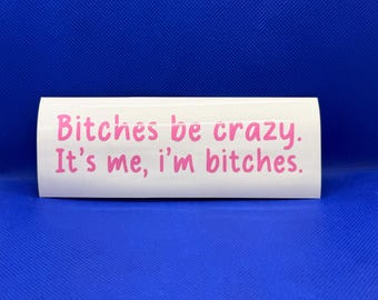 May include: A rectangular white vinyl decal featuring the pink text Bitches be crazy. It's me, i'm bitches. The lettering is presented in a rounded, casual font style, centered on the smooth surface of the sticker material.