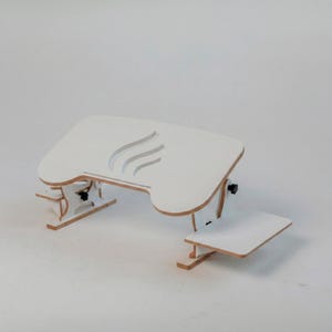 May include: A white, adjustable laptop desk with a curved design and a separate, smaller platform. The desk features a cutout design on the main surface and is constructed from light-coloured wood.