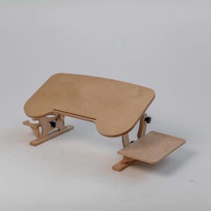 以下が含まれることがあります： 調整可能なデザインの明るい色の木製ラップトップデスク。 デスクは、湾曲したエッジを持つメインの表面と、より小さく、低いプラットフォームを備えています。 デスクは木製の脚と調整可能なジョイントで支えられています。