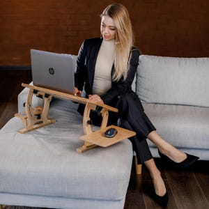 Puede incluir: Un soporte de escritorio ajustable para computadora portátil hecho de madera clara, con una plataforma principal para una computadora HP plateada y una plataforma lateral para un mouse. El soporte cuenta con bisagras y perillas mecánicas.
