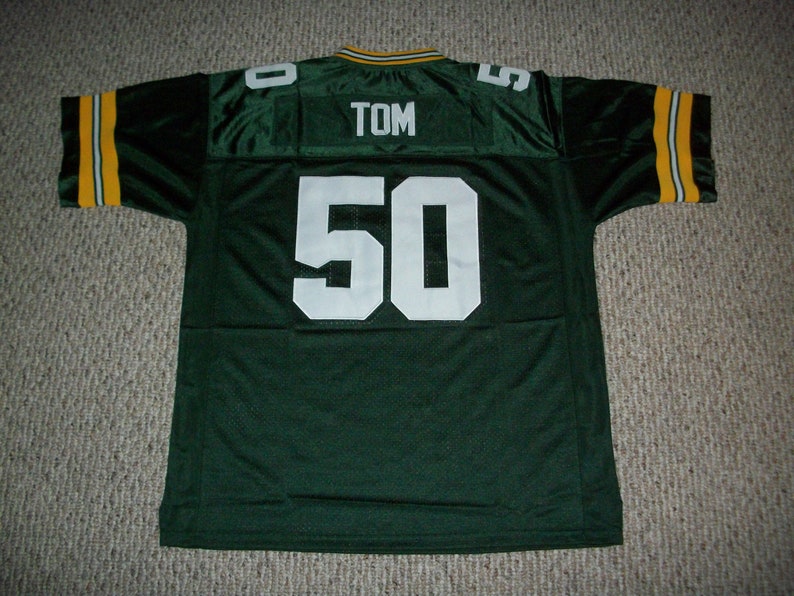 May include: Green football jersey with white lettering. The number 50 is on the back of the jersey with the name TOM above it.