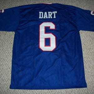 Pode incluir: Uma camisola de malha azul com o nome "DART" e o número "6" em branco com acabamento vermelho. As mangas têm o número "9". A camisola tem acabamentos vermelhos e brancos na gola e nas mangas.