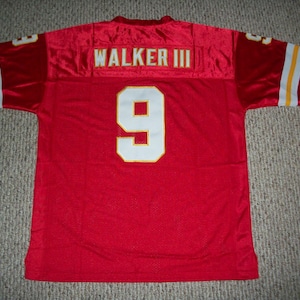 May include: Red football jersey with the name "WALKER III" across the shoulders and the number "9" on the back. The jersey has white and yellow stripes on the sleeves.