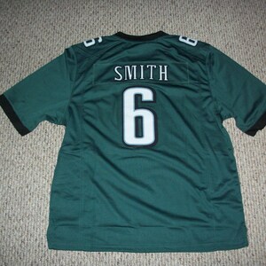 Puede incluir: Una camiseta de fútbol verde con el nombre "SMITH" y el número "6" en blanco. La camiseta tiene ribetes negros en las mangas y el cuello. La camiseta está hecha de un material transpirable.