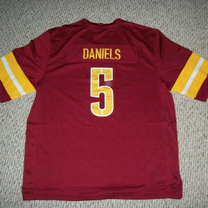 May include: A burgundy football jersey with gold and white stripes on the sleeves. The back of the jersey has the name "DANIELS" and the number "5" in gold.