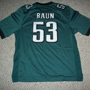 May include: A green football jersey with the name "BAUN" and the number "53" in white with a black outline. The jersey has black trim on the sleeves and collar.