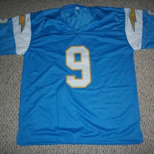 Puede incluir: Una camiseta de malla azul claro con el n&uacute;mero 9 en blanco con contorno dorado. La camiseta tiene detalles blancos y dorados en los hombros y las mangas, con un dise&ntilde;o de rayo. La camiseta est&aacute; tendida sobre una superficie alfombrada.