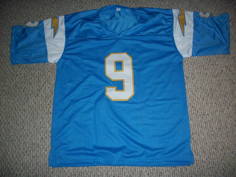 Puede incluir: Una camiseta de malla azul claro con el n&uacute;mero 9 en blanco con contorno dorado. La camiseta tiene detalles blancos y dorados en los hombros y las mangas, con un dise&ntilde;o de rayo. La camiseta est&aacute; tendida sobre una superficie alfombrada.