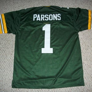 Può includere: Maglia da football verde con il nome "PARSONS" e il numero "1" in bianco. Le maniche hanno strisce gialle e bianche. La maglia è realizzata in materiale a rete.