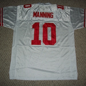 May include: White football jersey with red trim and the name "MANNING" and number "10" on the back.