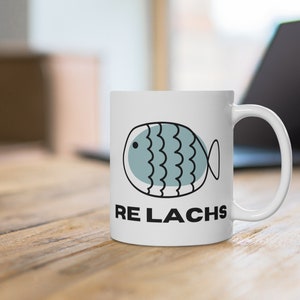 May include: White ceramic mug with a blue and black cartoon fish and the text "RE LACHs" printed on the front.