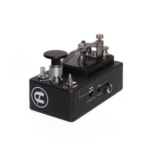 May include: A black electric guitar effects pedal with a silver lever and a black knob. The pedal has a white logo with the letter "E" and a lightning bolt. The text "BURST" and "CTRL" are printed on the pedal.