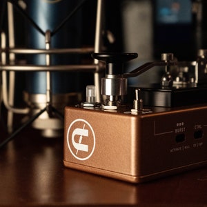 May include: A copper-colored guitar effects pedal with a white logo and a black knob. The pedal has a black control panel with a lever and two buttons. The text "OOO BURST CTRL" is printed on the pedal.