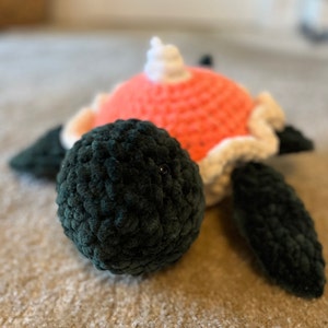 May include: A crocheted plush turtle toy with a pink shell, white accents, and black head and limbs.