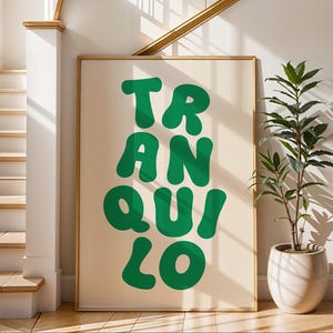 May include: A framed poster with the word "TRANQUILO" in large, green, bubble letters. The poster is displayed in a bright, well-lit hallway with a staircase and a potted plant.