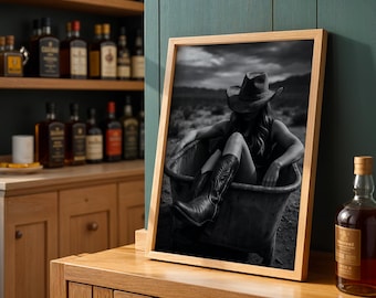 May include: Black and white framed print of a person in a cowboy hat and boots sitting in a metal tub. The print is displayed on a wooden cabinet, with bottles of liquor in the background.