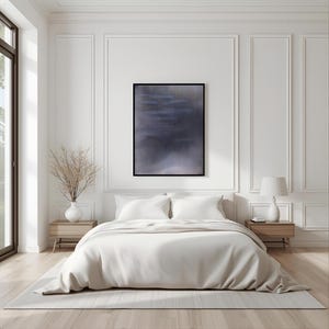 May include: A bedroom with a modern aesthetic. The focal point is a bed with white bedding and a beige blanket. Above the bed is a framed abstract art piece in shades of blue and gray. The room features light wood nightstands, a white lamp, and a vase with dried branches.