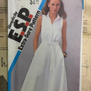 May include: A Simplicity ESP Extra-Sure Pattern 5690 for a sleeveless white collared dress with a button-down front, a tie-waist belt, and a full skirt. The pattern envelope is labelled size N, covering sizes 10, 12, and 14, and features a price of $1.50.