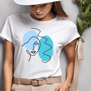 Peut inclure: T-shirt blanc avec un dessin abstrait au trait d'un visage de femme en bleu et turquoise.