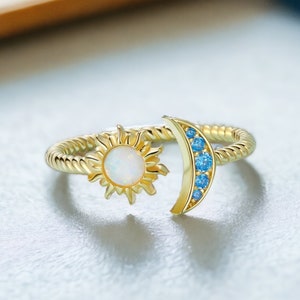 May include: Gold ring with a sun and moon design. The sun features a white opal stone and the moon is accented with blue gemstones.