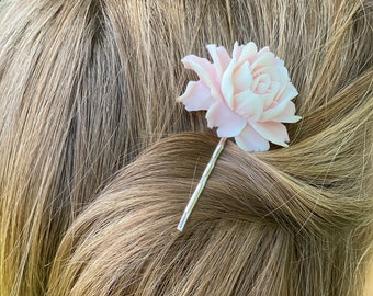 May include: A pink flower hair clip with a silver metal pin. The flower is made of a soft, pliable material and has a delicate, feminine look.