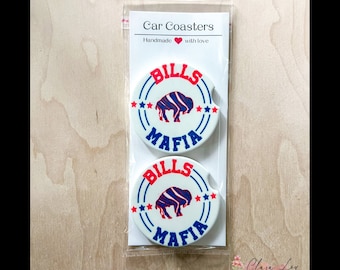 May include: Two white round car coasters with a blue and red buffalo design. The coasters have the words "Bills Mafia" printed on them. The coasters are packaged in a clear plastic bag with a white card that says "Car Coasters" and "Handmade with love".