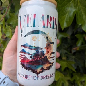 Peut inclure: Gobelet blanc avec un couvercle en bambou et une paille. Le gobelet porte le mot "VELARIS" dans une police stylisée, au-dessus d'une scène de paysage avec un croissant de lune et le texte "COURT OF DREAMS".