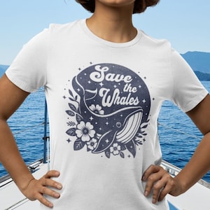 以下が含まれることがあります： 青いクジラのグラフィックと「Save the Whales」というレトロなフォントのテキストが書かれた白いTシャツ。クジラは花と星に囲まれています。