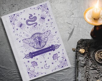 Puede incluir: Un libro blanco titulado INCANTATIONS con ilustraciones en tinta morada de una polilla, serpiente, ojos y estrellas. A su lado hay un libro negro texturizado con detalles dorados, un cristal transparente y una vela encendida.