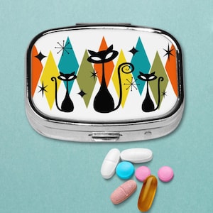 May include: A silver pill box with a retro design featuring black cat silhouettes and colorful geometric shapes. Several pills of various colors and shapes are scattered below the box, suggesting a medication organizer.
