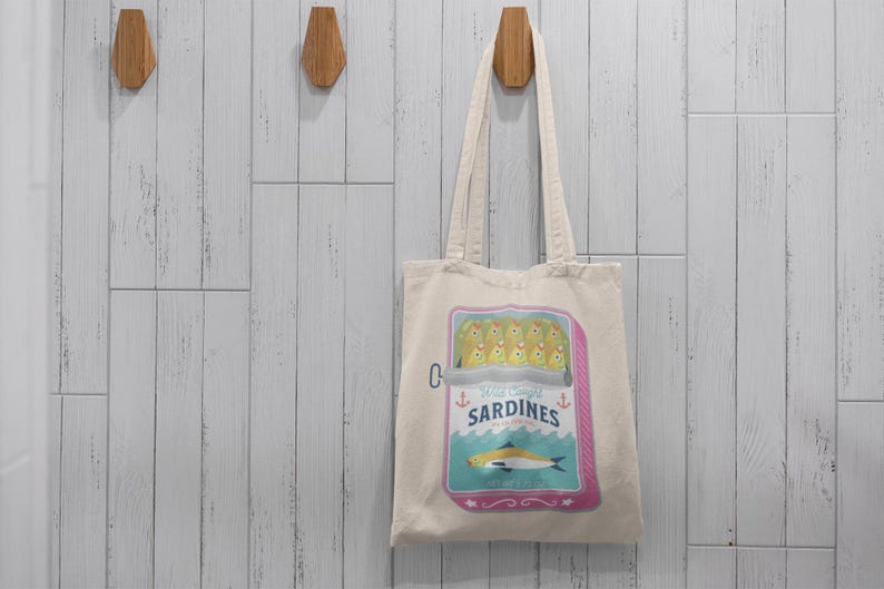 May include: A white canvas tote bag with a colorful illustration of a can of sardines. The can has a pink label with the text "Wild Caught Sardines" and a blue and white illustration of a fish.
