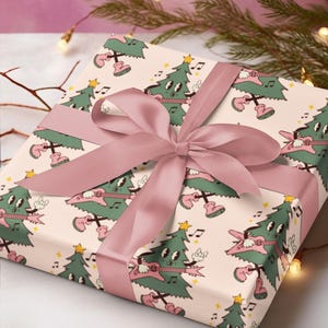 May include: A pink gift box with a white background and a pattern of green Christmas trees playing electric guitars. The box is tied with a pink satin ribbon.