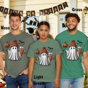 Puede incluir: Tres personas con camisetas con un fantasma de dibujos animados que lleva un gorro y sostiene una calabaza y una taza de caf&eacute;. Las camisetas son de tres colores diferentes: verde musgo, verde claro y verde hierba. El texto "Trick or Treat?" est&aacute; en una pancarta sobre las personas.