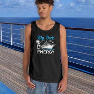 May include: Black tank top with the words "Big Deck Energy" in turquoise script above a white illustration of a cruise ship, palm trees, and the word "ENERGY" in white block letters. The tank top is worn by a person on a cruise ship deck.