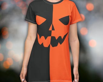 Puede incluir: Vestido de manga corta con un diseño de cara de calabaza de Halloween. El vestido está dividido verticalmente, un lado negro y el otro naranja. La cara de la calabaza tiene ojos triangulares y una boca dentada.