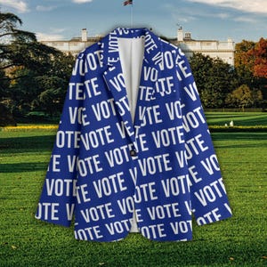 May include: A blue blazer with the word "VOTE" in white repeated across the fabric. The blazer has a single black button and a white interior. The background features a grassy lawn and a building with a flag.