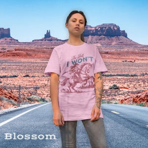 May include: A pink t-shirt with a graphic of a woman riding a horse. The text on the shirt reads "The Hell I Won't".