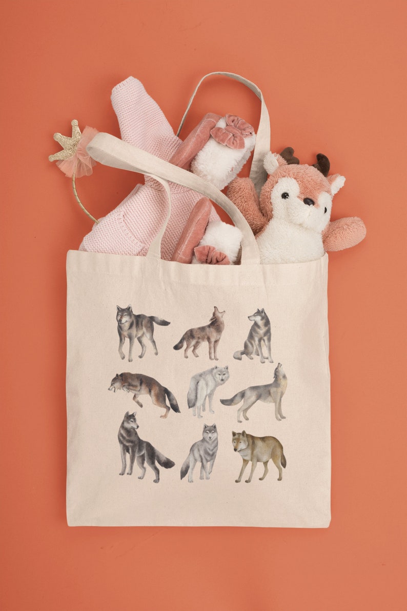 May include: A beige canvas tote bag featuring a design of various wolves in different poses. The bag is filled with a pink sweater, a stuffed deer, and a pink headband with a gold crown.