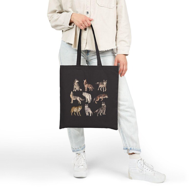 May include: A black tote bag featuring a design of nine different wolves in various poses. The wolves are depicted in shades of brown, grey, and white.
