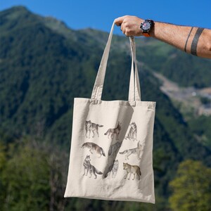 May include: A beige tote bag featuring a design of several wolves in various poses. The wolves are depicted in a watercolour style and are in shades of grey and brown.