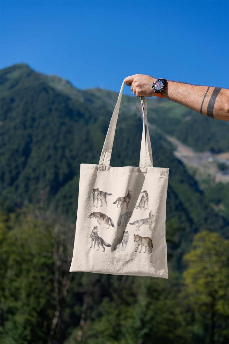 May include: A beige tote bag featuring a design of several wolves in various poses. The wolves are depicted in a watercolour style and are in shades of grey and brown.