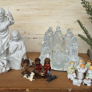 May include: A collection of ceramic and glass nativity figurines. The set includes figures of Mary, Joseph, baby Jesus, angels, and the three wise men. The figurines are in various colors and styles, creating a traditional Christmas display.