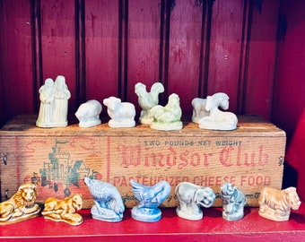 May include: A collection of 10 miniature figurines, including a rooster, a goose, a lion, a rhino, an elephant, a horse, a sheep, a pig, and two people. The figurines are made of ceramic and are painted in various colors. The figurines are arranged on a wooden shelf with a wooden box in the background. The box has the text "Windsor Club" printed on it.