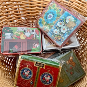 May include: A collection of four decks of playing cards in plastic packaging. One deck features Santa Claus at a desk, another shows blue and white flowers with the text Stardust, one displays red pocket watches, and one depicts a koala on a branch.