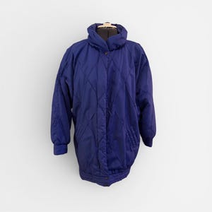 Puede incluir: Chaqueta vintage acolchada azul marino con cuello alto y cierre de botones. La chaqueta tiene un patrón de diamantes y dos bolsillos laterales. Las mangas tienen puños elásticos. La chaqueta se muestra en un maniquí.