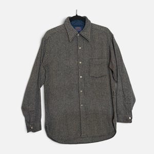 May include: A long-sleeve button-down shirt in a dark gray and black micro-patterned fabric. The shirt features a pointed collar, a single chest pocket on the left side, light-colored buttons, and a dark blue quilted lining visible at the inner neck.