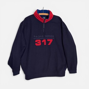 May include: A navy blue long-sleeve pullover sweatshirt featuring a quarter-zip closure with a red and blue stand-up collar. The front displays the embroidered text RACING SERIES above the large red numbers 317 and a small GAP logo at the neck.